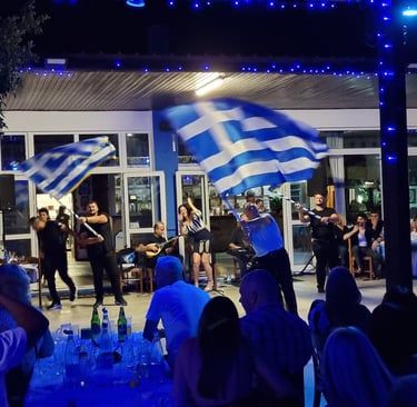 Greek dancers waving flags at a traditional night festival with live bouzouki music.