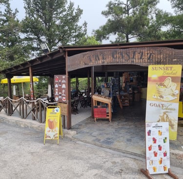 Rustic outdoor cafe and souvenir shop in Greece with wooden architecture and menu signs for local snacks.
