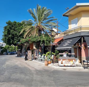Sunny street in Lardos, Rhodes, featuring a crepe stand and outdoor cafes under palm trees.