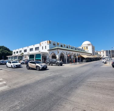 Historic white street market building with domed roof in Rhodes, Greece under a bright blue sky.