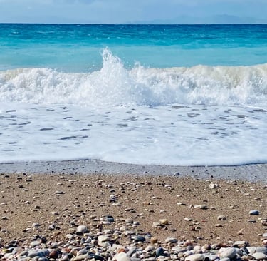 Turquoise ocean waves crashing on a pebbled sandy beach under a clear blue sky.