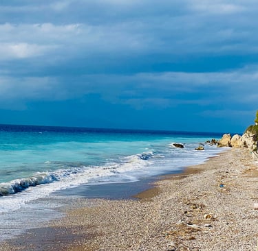 Pebble beach with turquoise ocean waves under a dramatic cloudy blue sky.