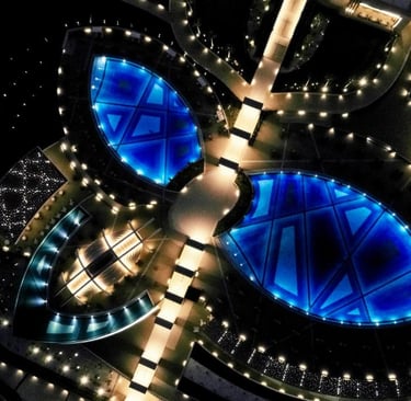 Aerial night view of a luxury resort with illuminated blue swimming pools and geometric walkways.