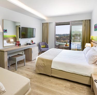 Modern hotel room with king bed, desk, wall-mounted TV, and private balcony with a scenic view.