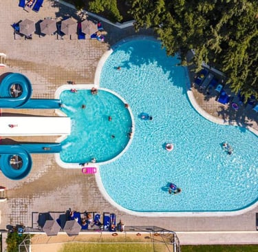 Aerial view of a luxury resort swimming pool with blue water slides and guests relaxing on lounge chairs.