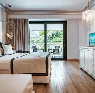 Luxury hotel room with a plush white bed, hardwood floors, and a private balcony overlooking green foliage.