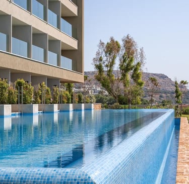 Luxury hotel infinity pool with blue tiles overlooking a lush garden and modern building balconies.