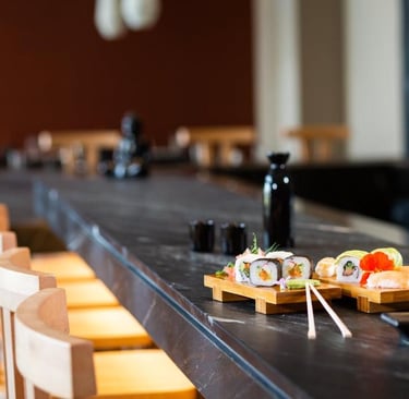 Fresh sushi rolls and nigiri served on wooden platters at a modern dark stone restaurant bar.