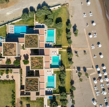 Aerial view of a luxury beachfront resort with private pools and white umbrellas on a sandy shore.