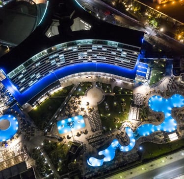 Aerial night view of a luxury resort with illuminated swimming pools and modern architecture.