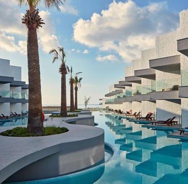 Luxury modern beachfront resort with swim-up suites, infinity pool, and palm trees under a blue sky.