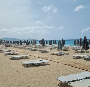 Empty sunbeds and closed grey umbrellas on a sandy tropical beach with blue ocean water.