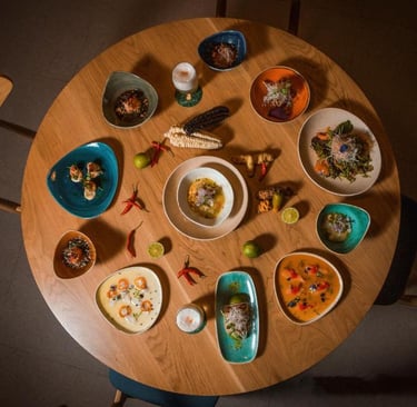 Overhead view of a round wooden table featuring various colorful Peruvian ceviche dishes and tapas.