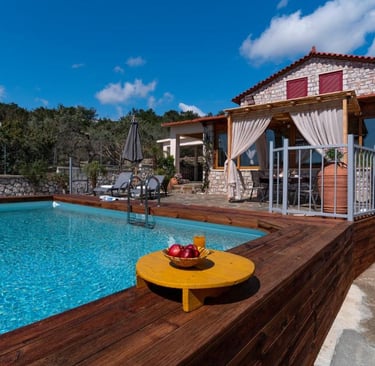 Luxury stone villa with a private swimming pool, wooden deck, and outdoor patio under a blue sky.