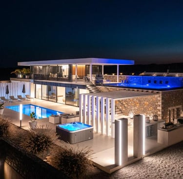 Luxury modern villa at night with illuminated swimming pools, hot tub, and outdoor lounge areas.