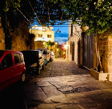 Cars parked along a cobblestone street in a historic European town at twilight.