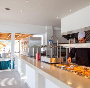 Professional chef serving hot food at a bright resort buffet station with outdoor seating.