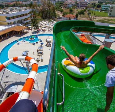 A girl on an inflatable ring slides down a green water slide at a sunny summer resort waterpark.
