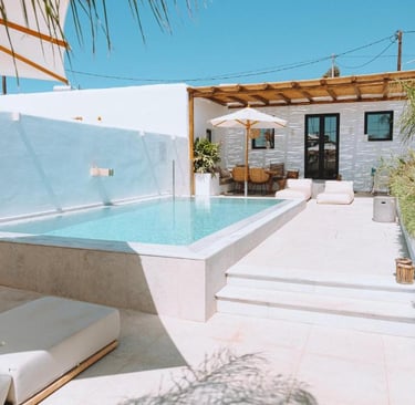 Luxury villa patio with a private swimming pool, white lounge chairs, and an outdoor terrace under a clear blue sky.