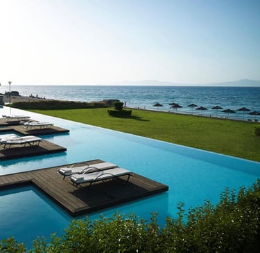 Luxury infinity pool with wooden sun decks and lounge chairs overlooking a beach and ocean.