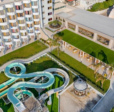 Aerial view of a luxury family resort featuring a large hotel building, outdoor water slides, and a rooftop garden.