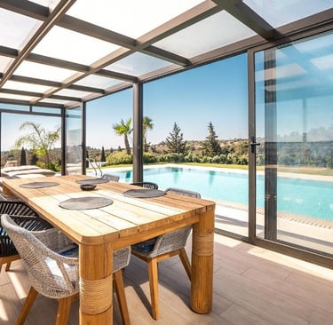 Luxury sunroom with a wooden dining table overlooking a backyard swimming pool and scenic landscape.