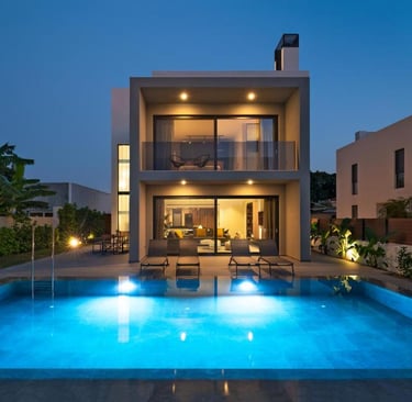 Modern luxury villa at twilight with a glowing blue swimming pool and outdoor lounge area.