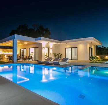 Modern luxury villa at night with a glowing swimming pool and outdoor lounge patio area.