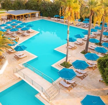 Aerial view of a luxury resort swimming pool with blue umbrellas, palm trees, and lounge chairs.