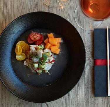 Fresh white fish ceviche served with cherry tomatoes and melon in a black bowl with rose wine.