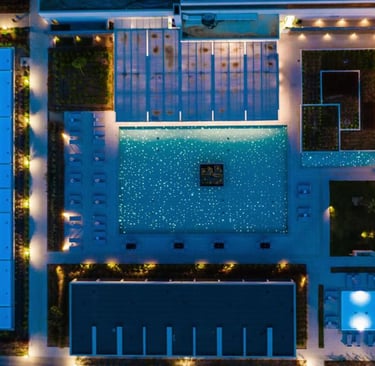 Aerial view of a luxury resort pool illuminated at night with fiber optic starry lights.