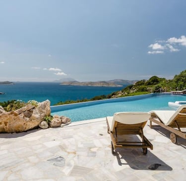 Luxury infinity pool and sun loungers overlooking the Mediterranean Sea and Greek islands.