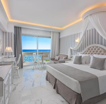 Luxury hotel room with a sea view balcony, marble floors, and elegant canopy bed.