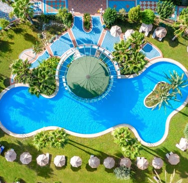 Aerial view of a Atrium Palace swimming pool with palm trees, sun loungers, and blue water.