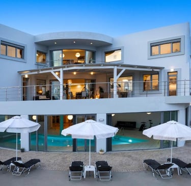 Luxury modern villa with a private swimming pool, sun loungers, and patio umbrellas at dusk.