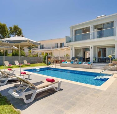 Modern luxury villa with a private swimming pool, sun loungers, and patio umbrellas on a sunny day.
