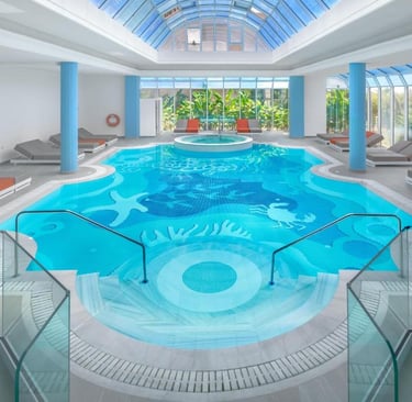 Luxury indoor swimming pool with sea creature mosaic tiles, glass skylight, and lounge chairs.