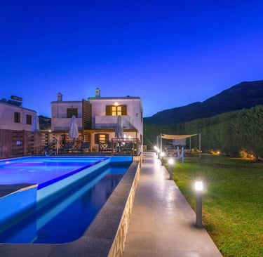 Luxury villa with illuminated private swimming pool and garden at night under a blue sky.