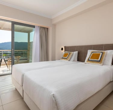 Modern hotel room with twin beds and a private balcony overlooking scenic mountains.
