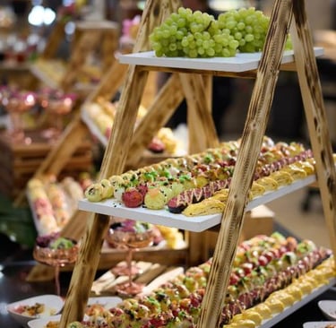Elegant tiered wooden ladder display featuring assorted gourmet sushi rolls and fresh green grapes at a buffet.