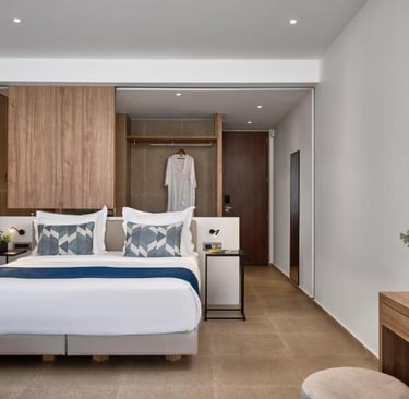 Modern hotel suite with a king-sized bed, white linens, blue accents, and a contemporary wood desk.