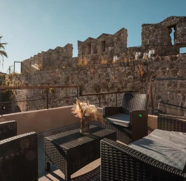 Luxury patio furniture on a sunlit terrace overlooking a historic stone castle wall and palm tree.