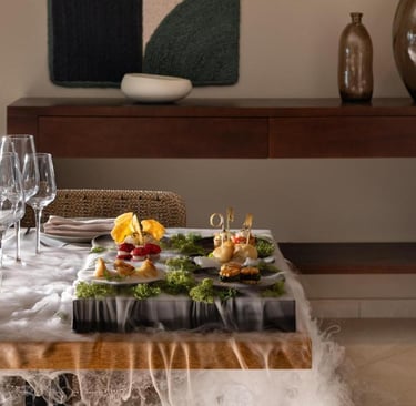 Elegant fine dining appetizers served with dry ice mist on a wooden table with wine glasses.