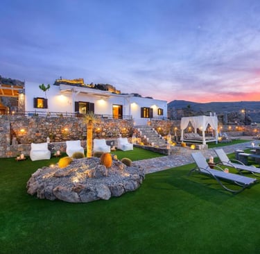 Luxury Mediterranean villa with stone walls, garden lounge, and sunset view over hills.