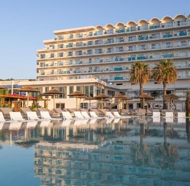 Luxury beach resort hotel with a reflection in the swimming pool, lounge chairs, and palm trees.