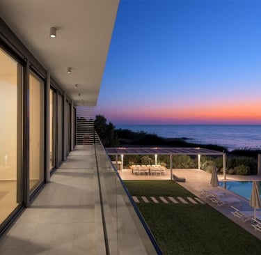 Luxury modern villa balcony overlooking a swimming pool and ocean at sunset.