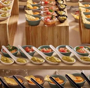 Gourmet catering appetizers featuring individual servings of guacamole, salsa, and cheese dip on bamboo platters.