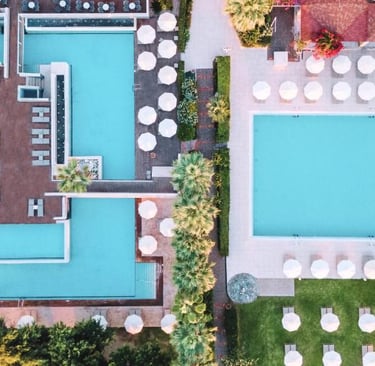 Aerial view of a luxury hotel resort featuring turquoise swimming pools, white sun umbrellas, and palm trees.