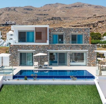 Luxury stone villa with a private infinity pool and sun loungers overlooking a mountain in Greece.