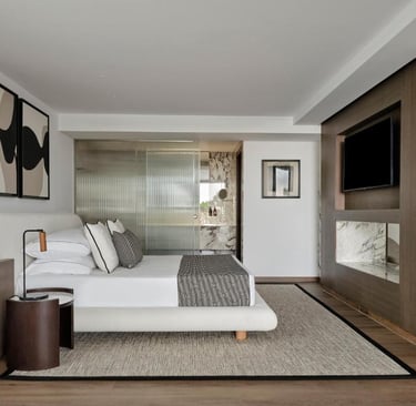 Modern luxury hotel bedroom with a minimalist white bed, wooden wall paneling, and an ensuite marble bathroom.